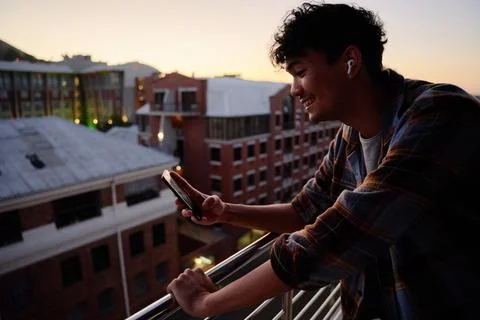 Profile view of young multiracial man in shirt smiling while using phone on Stock Photos