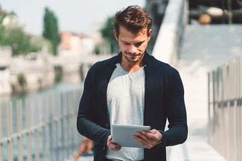 Profile of young man looking down at the digital tablet in his hands, while Stock Photos