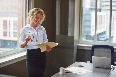 Profit is proof of her career commitment. a businesswoman reading a report in an Stock Photos