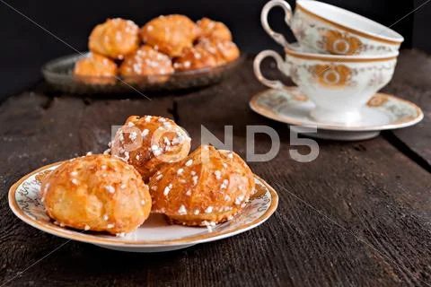 Profiteroles topped with sugar and vintage cup with tea on a dark background Stock Photos
