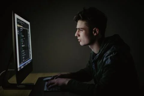 Program development concept. Young man working with computer in dark room. Foto stock
