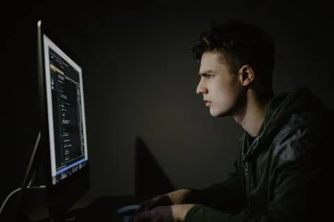 Program development concept. Young man working with computer in dark room. Stock Photos
