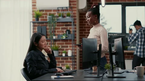 Programer standing up holding digital tablet talking with coder sitting at desk Stock Footage 168252057