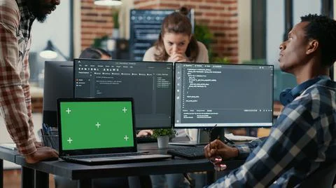 Programer taking glasses off talking with colleague at desk with laptop with 스톡 사진