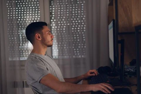 Programer working on his computer while the screen light reflects on his face Stock Photos