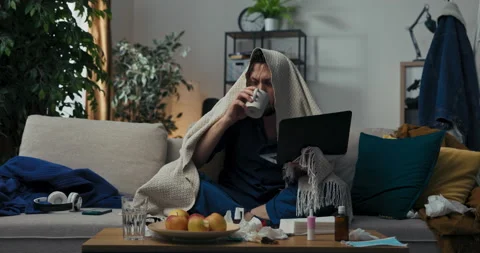 Programmer with beard is sitting on sofa and holding laptop. He is sick and has Stockbeeldmateriaal 218331784