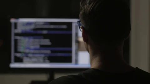 Programmer from behind and programming code on computer monitor at night in a Stock Footage 84710997