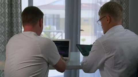 A programmer codes while a colleague suggests fixes from a tablet. 스톡 동영상 294298730