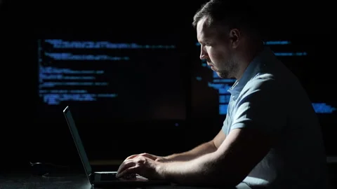Programmer coding on laptop in dark room. Programmer typing beside blue source Video stock 344516445