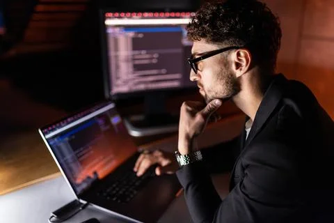 Programmer coding on a laptop in the dark with a view of the lights of the ni Stockfoto's