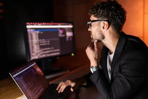 Programmer coding on a laptop in the dark with a view of the lights of the ni Stock Photos