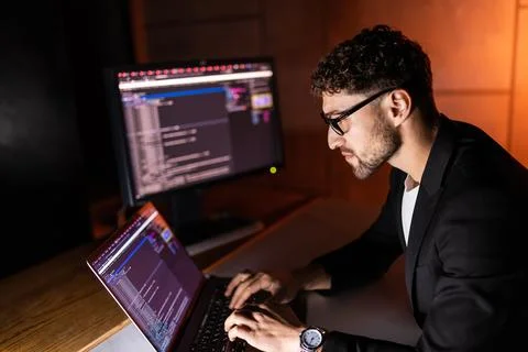 Programmer coding on a laptop in the dark with a view of the lights of the ni Stock Photos