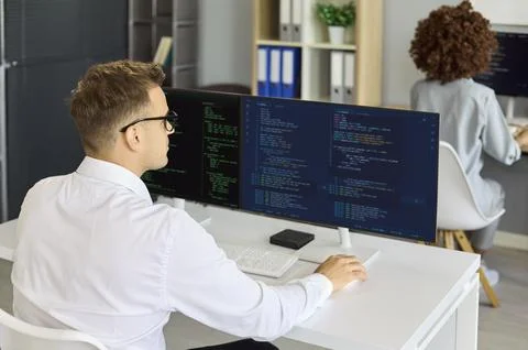 Programmer coding on wide monitor in office, focused software workflow Stock Photos