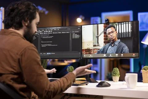 Programmer doing software debugging helped by coworker in videocall Fotos de archivo