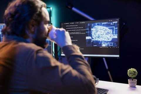 Programmer drinking coffee and doing maintenance on AI systems Stock Photos