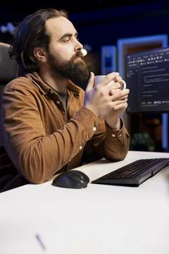 Programmer drinking coffee and writing lines of code filtering malicious traffic Stock Photos