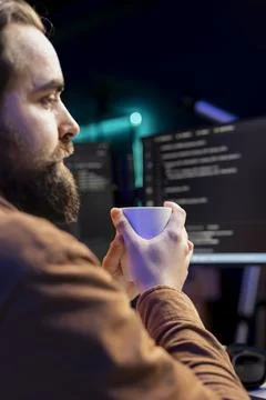 Programmer drinking cup of coffee in the morning while building firewalls Foto stock