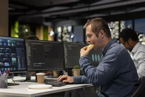 Programmer eating croissant in startup office Stock Photos