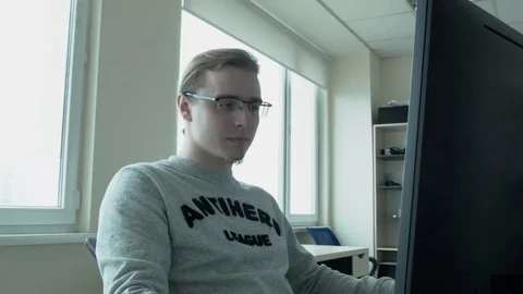 A programmer with glasses and a gray jacket with an anti-hero inscription looks Stock Footage 74699240
