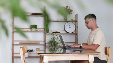 A programmer in glasses works from home in a large, bright living room. Stock Footage 310219471