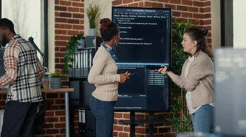 Programmer holding digital tablet analyzing code on wall screen tv while Stock Photos