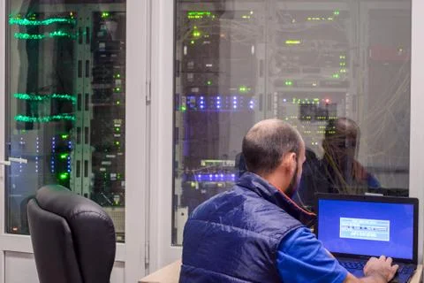 A programmer  with a laptop sits in front of the glass door of the server roo 库存照片