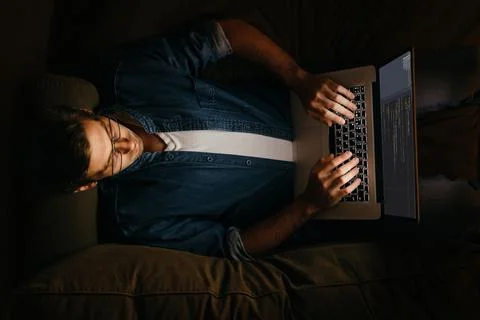 Programmer laying on sofa and working at his laptop Stock Photos
