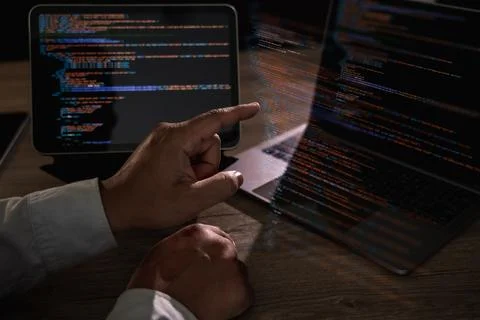 Programmer pointing at laptop screen with visible lines of code and tablet .. 스톡 사진