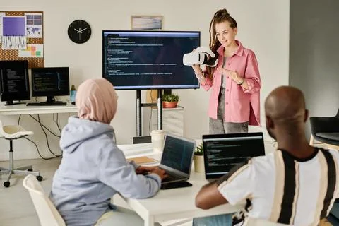 Programmer presenting VR glasses to her colleagues Foto stock