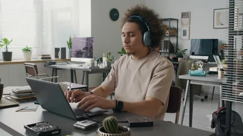 Programmer Putting on Headphones while Writing Code on Laptop in Office Stock-Footage 299272402