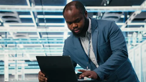 Programmer at server farm workplace desk using laptop, doing network management Stock Footage 330205891