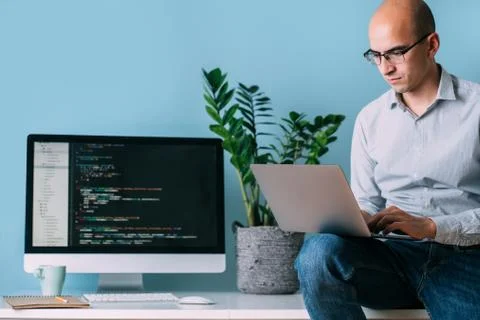 Programmer is sitting on desk, working analysing code on the laptop. 스톡 사진