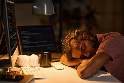 Programmer sleeping at his workplace in dark office Stock Photos