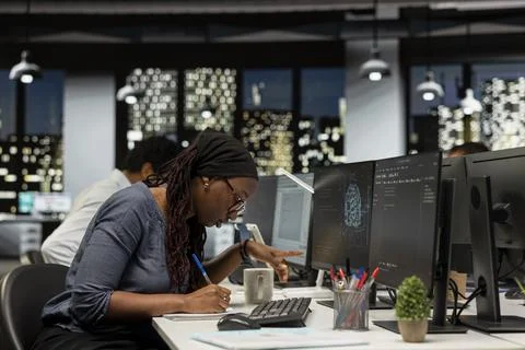 Programmer taking notes at office desk, reviewing AI system metrics 写真素材