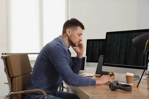 Programmer talking on phone while working at desk in office Foto stock
