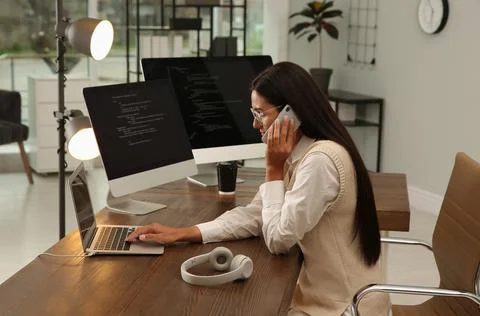 Programmer talking on phone while working at desk in office Stock Photos