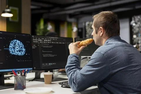 Programmer in tech startup office eating croissant and automating tasks with AI 写真素材