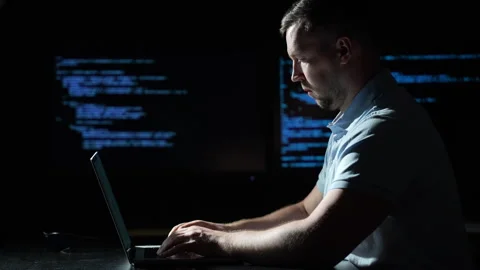 Programmer types code on laptop in darkness. Programmer works beside illuminated Stock Footage 344077563