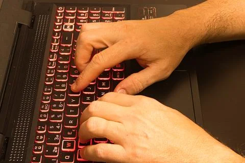 Programmer typing on a laptop with backlit red keyboard Stock Photos