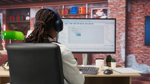 Programmer wearing headphones types code into PC, developing software Stock Photos