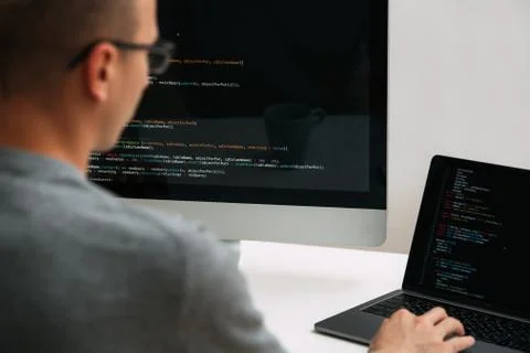 Programmer, working behind the desk, analysing code on the black screen. 库存照片