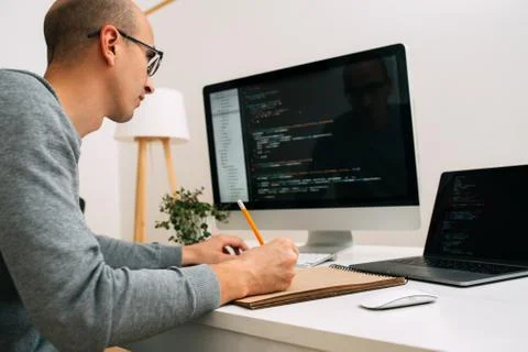 Programmer, working behind the desk, analysing code on the black screen. 库存照片