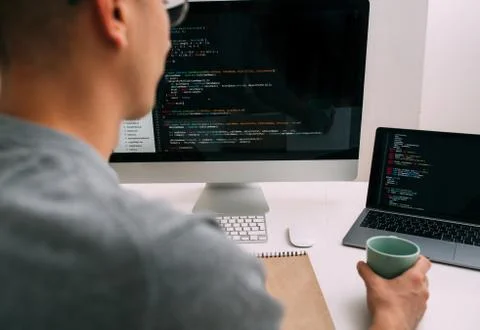 Programmer, working behind the desk, analysing code on the black screen. Stock Photos