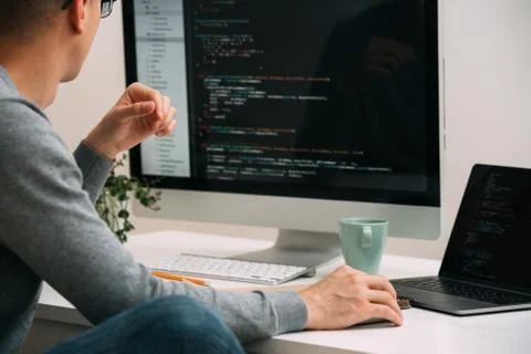 Programmer, working behind the desk, analysing code on the black screen. Stock Photos