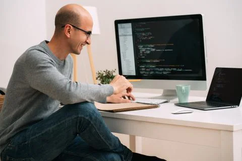 Programmer, working behind the desk, analysing code on the black screen. Stock Photos