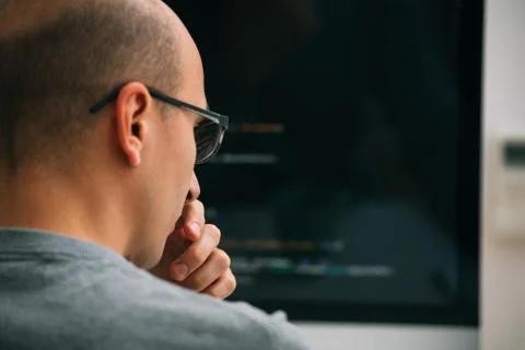 Programmer, working behind the desk, analysing code on the black screen. Stock Photos