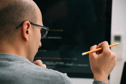 Programmer, working behind the desk, analysing code on the black screen. Stock Photos