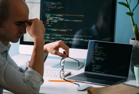 Programmer, working behind the desk, analysing code on the black screen. Stock Photos