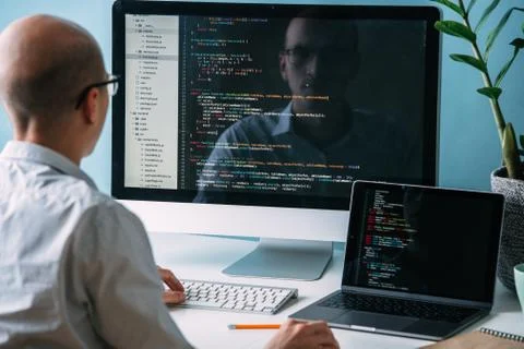 Programmer, working behind the desk, analysing code on the black screen. Stock Photos