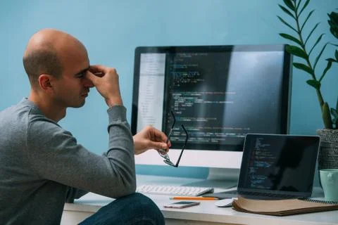 Programmer, working behind the desk, analysing code on the black screen. Stock Photos